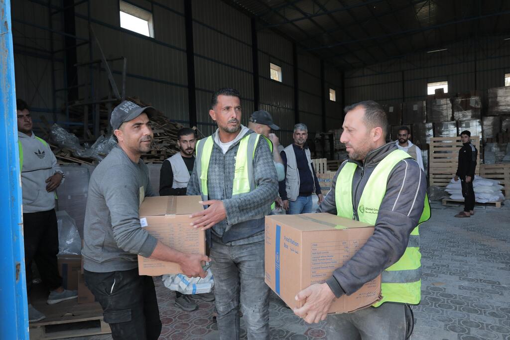 Des hommes en gilets jaunes transportent des cartons d'aide alimentaire à l'intérieur d'un entrepôt lors d'une distribution.