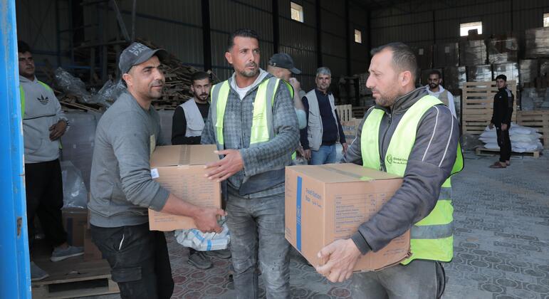 Dos hombres con chalecos de seguridad sostienen cajas de suministros alimentarios en un almacén