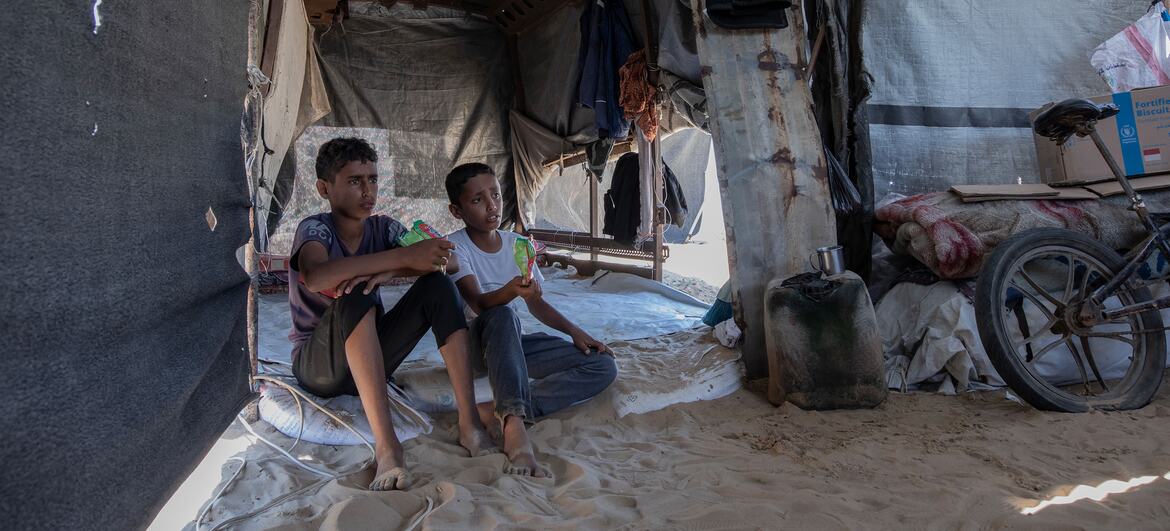 Two young boys sitting inside a makeshift tent in Al-Mawasi, Gaza.