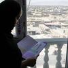 14-year-old Afghan girl Rabia reads a textbook by a window overlooking a cityscape.