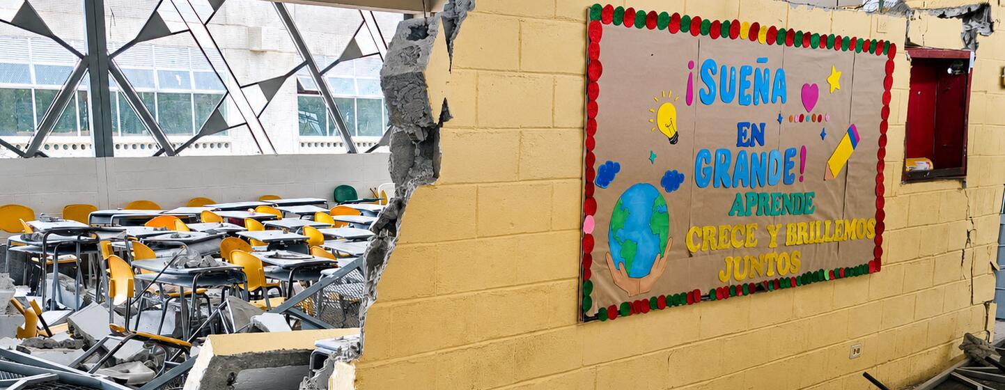 Un aula dañada en la escuela industrial La Carrasquilla en Quibdó, Colombia, donde se puede ver una pared de ladrillos amarillos derrumbada y escombros esparcidos entre los pupitres volcados.
