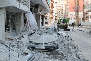 A crushed car lies under piles of concrete rubble and debris on a street in Tyre, Lebanon, following an airstrike.