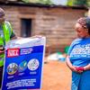 Lors d'une campagne de sensibilisation communautaire en République démocratique du Congo, une employée de UNICEF montre une affiche éducative « STOP EBOLA » à une femme tenant un enfant.