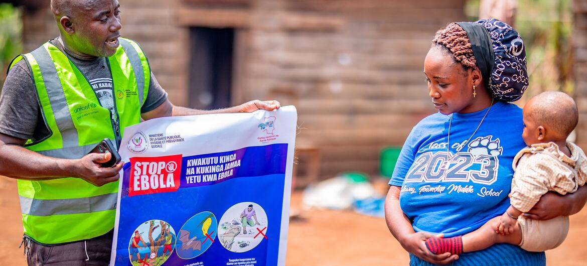 Uma funcionária do Unicef mostra um cartaz educativo com a mensagem "PARE O EBOLA" para uma mulher que segura uma criança durante um evento de conscientização comunitária na República Democrática do Congo.