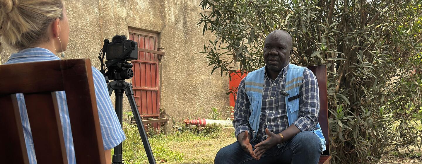 Emmanuel Madragule est assis à l'extérieur pendant qu'il est interviewé par une journaliste munie d'une caméra à Bunia, dans l'Ituri, en République démocratique du Congo.