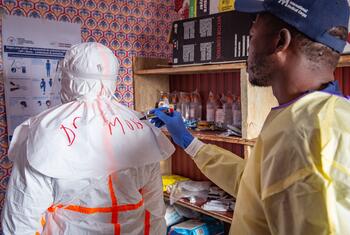 A health worker writes 'Dr. Moise' on the back of another person wearing white PPE in a clinic.