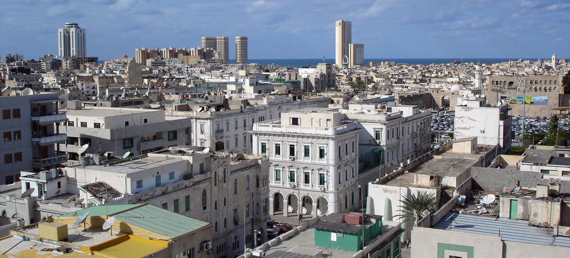 A panoramic view of Tripoli, Libya, showing a dense mix of buildings and the Mediterranean Sea in the background.