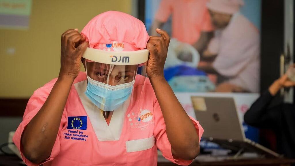 Mfanyakazi wa afya mwanamke katika Jamhuri ya Kidemokrasia ya Kongo akirekebisha ngao yake ya uso na barakoa wakati wa kukabiliana na mlipuko wa Ebola.