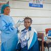 Une sage-femme soutenue par l'UNFPA, vêtue d'une tenue de protection bleue, prend la température d'une femme dans un centre de santé du camp de déplacés de Kigonze.