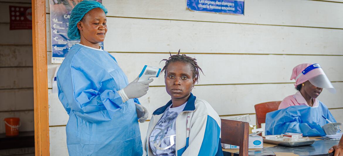 Une sage-femme soutenue par l'UNFPA, vêtue d'une tenue de protection bleue, prend la température d'une femme dans un centre de santé du camp de déplacés de Kigonze.