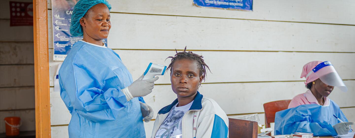 Une sage-femme soutenue par l'UNFPA, vêtue d'une tenue de protection bleue, prend la température d'une femme dans un centre de santé du camp de déplacés de Kigonze.