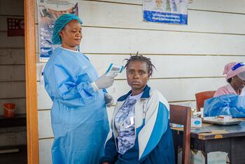 Une sage-femme soutenue par l'UNFPA, vêtue d'une tenue de protection bleue, prend la température d'une femme dans un centre de santé du camp de déplacés de Kigonze.