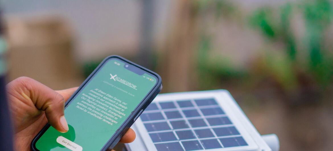 A person's hand holding a smartphone displaying the StartGrow app next to a solar-powered agricultural sensor.