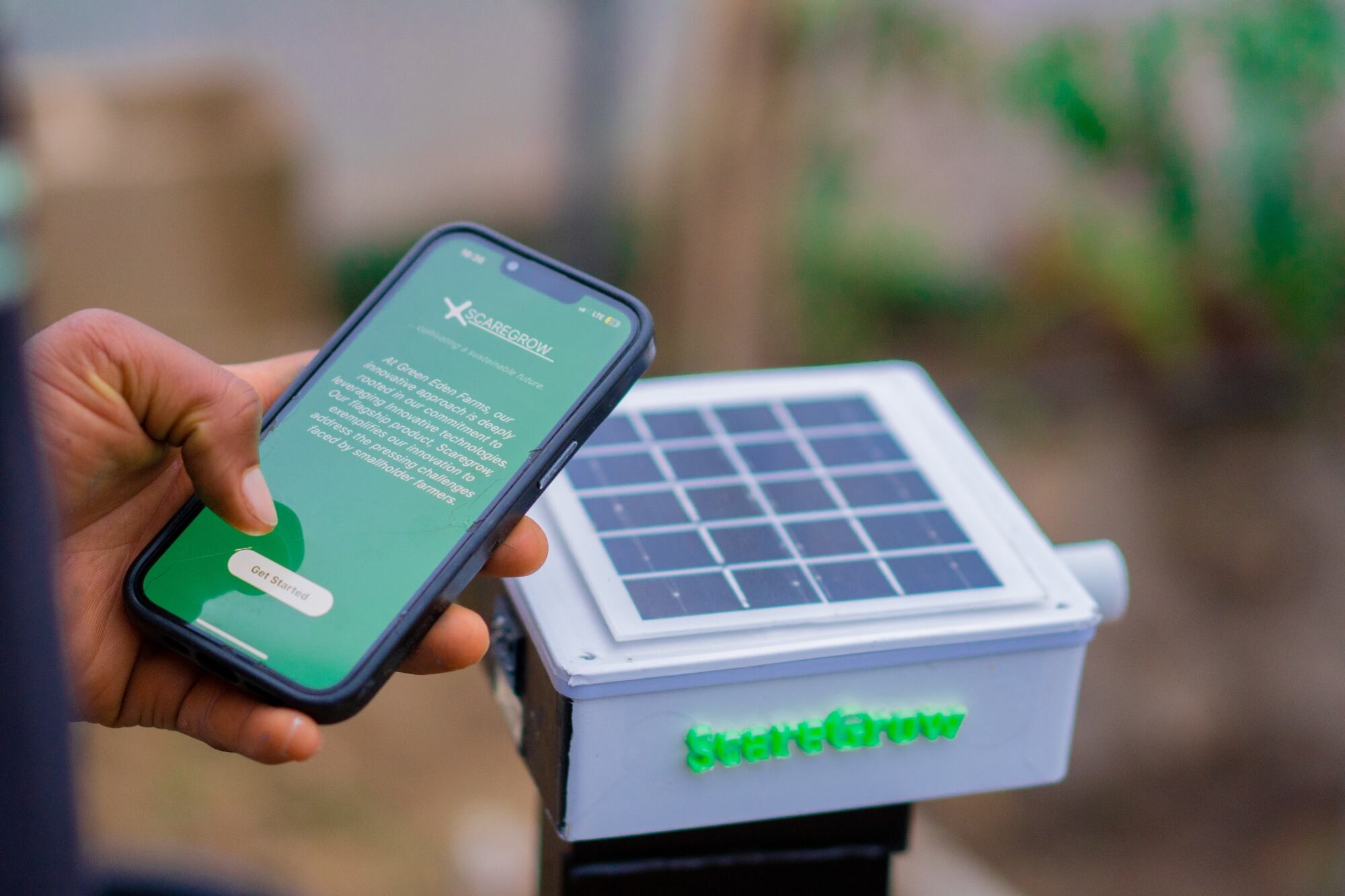 Una mano sostiene un teléfono inteligente con la aplicación StartGrow instalada, junto a un sensor agrícola alimentado por energía solar.