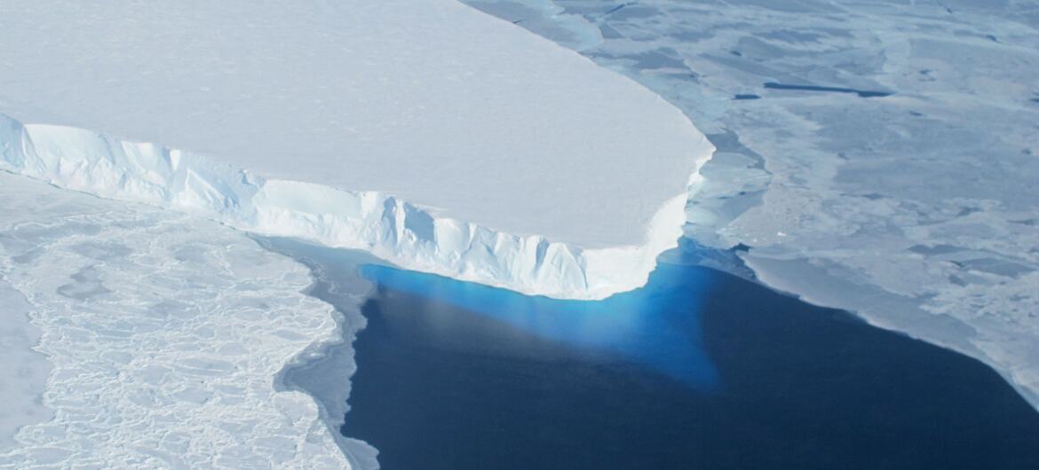 Aerial view of the Thwaites Glacier in Antarctica showing a large section of an ice shelf with deep blue water beneath it.