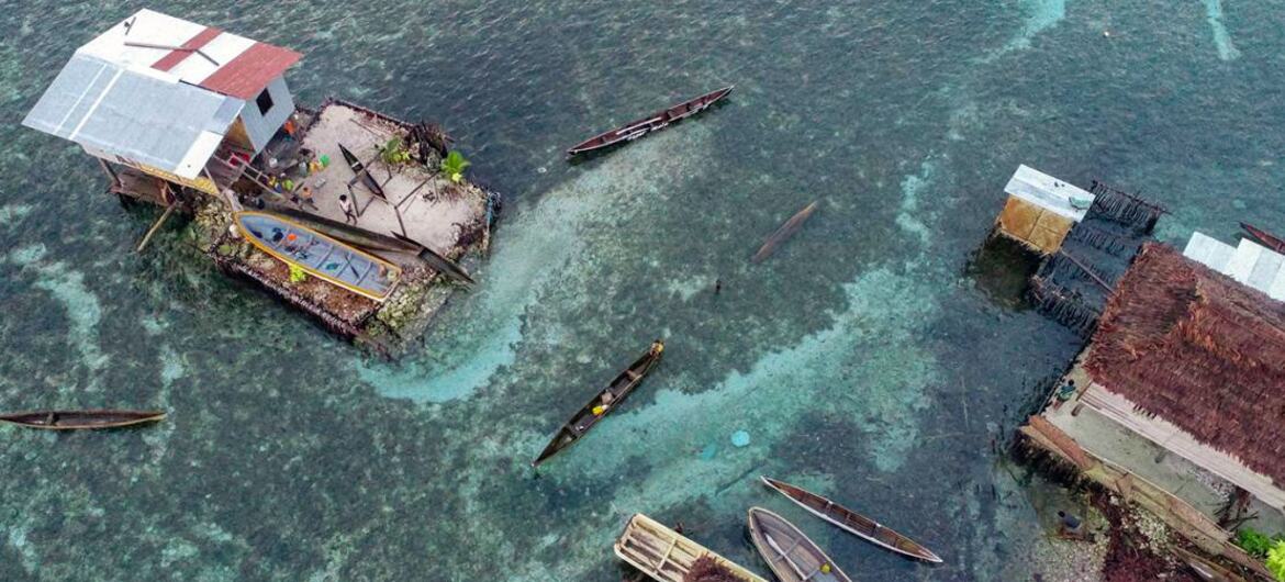 Vista aérea de casas sobre pilotes y embarcaciones tradicionales en un pueblo costero de Papúa Nueva Guinea.