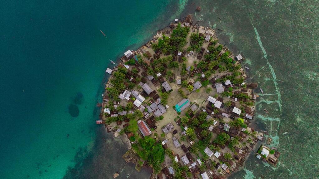Mtazamo wa angani wa kijiji cha pwani kwenye kisiwa huko Papua New Guinea, kilichozungukwa na maji ya zumaridi.