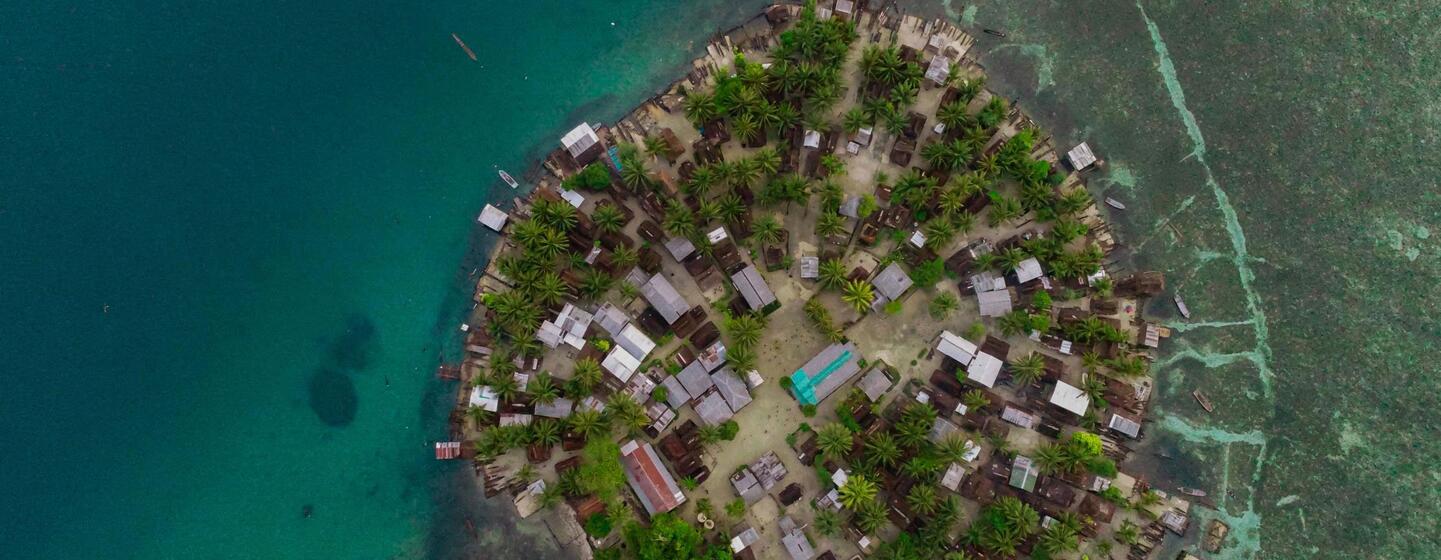 Vue aérienne d'un village côtier sur une île de Papouasie-Nouvelle-Guinée, entouré d'eaux turquoise.