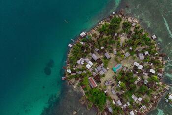 Vue aérienne d'un village côtier sur une île de Papouasie-Nouvelle-Guinée, entouré d'eaux turquoise.