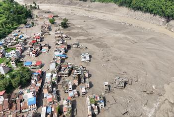 Aerial view of a mud-covered settlement in Rasuwa District, central-northern Nepal, with damaged buildings beside a silt-filled riverbed after flash floods.