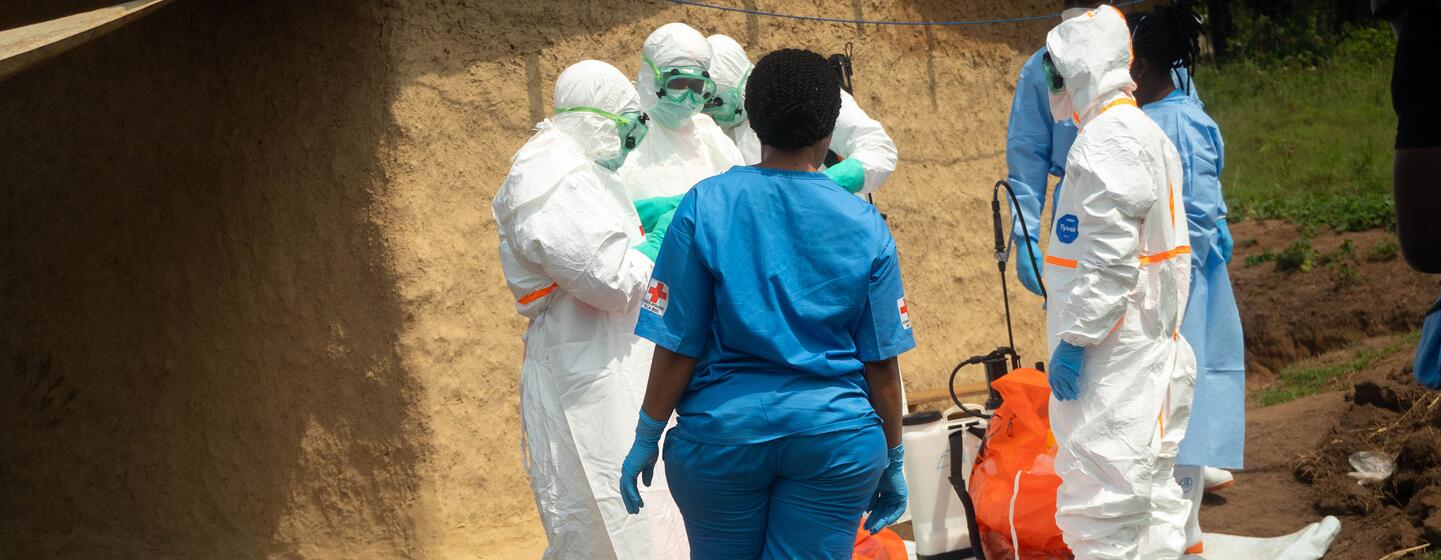 Des volontaires de la Croix-Rouge entièrement vêtus d'équipements de protection individuelle blancs et une infirmière en blouse bleue procèdent à l'inhumation sécurisée d'un nourrisson à Bembei, dans l'Ituri, en RDC, lors d'une épidémie d'Ebola.