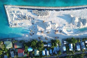 Coastal protection  in Tuvalu showing sandbags and earthworks forming a protective barrier along the turquoise shoreline next to a small village.