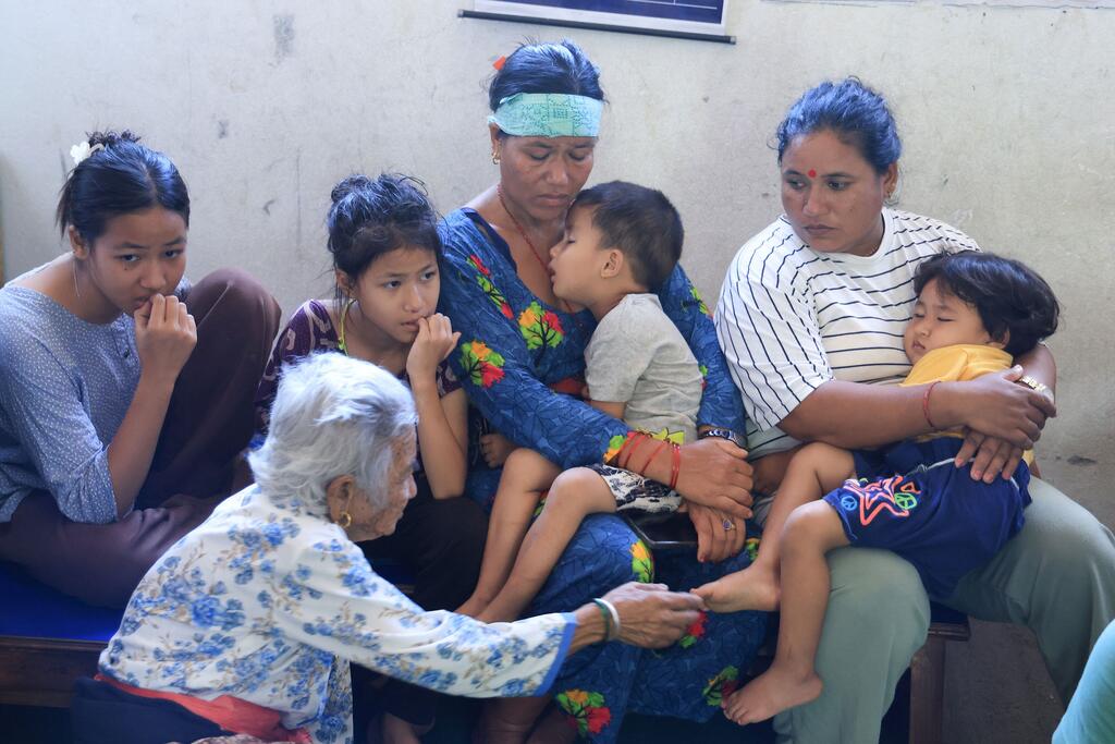 Une famille népalaise de six personnes, comprenant une femme âgée et plusieurs jeunes enfants, est assise sur un banc à l'intérieur d'une école du district de Nuwakot, au Népal, après avoir été déplacée de son domicile par les inondations.