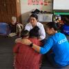 Un trabajador de UNICEF , vestido con una camisa azul, consuela a una mujer angustiada que sostiene a dos niños en el suelo de un refugio en Nuwakot, Nepal, mientras una anciana y otro adulto observan la escena.
