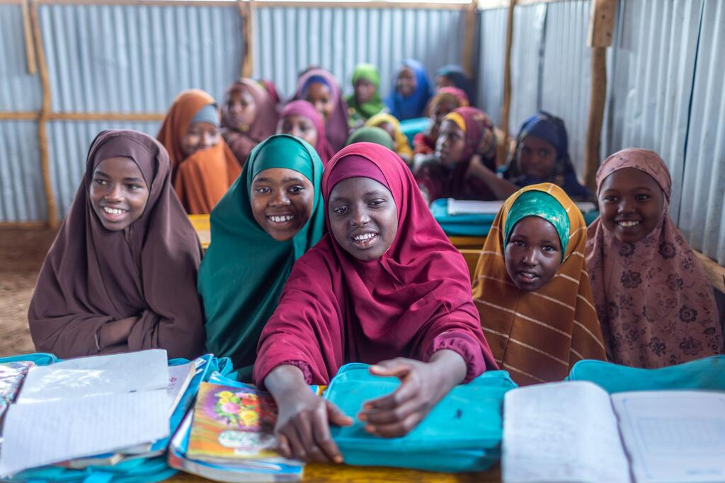 Wasichana wa Kisomali waliovalia vitambaa vya rangi mbalimbali vichwani wamekaa kwenye madawati yenye vitabu na folda za bluu ndani ya darasa la shule ya Waaberi IDP linalofadhiliwa na UNICEF huko Baidoa.