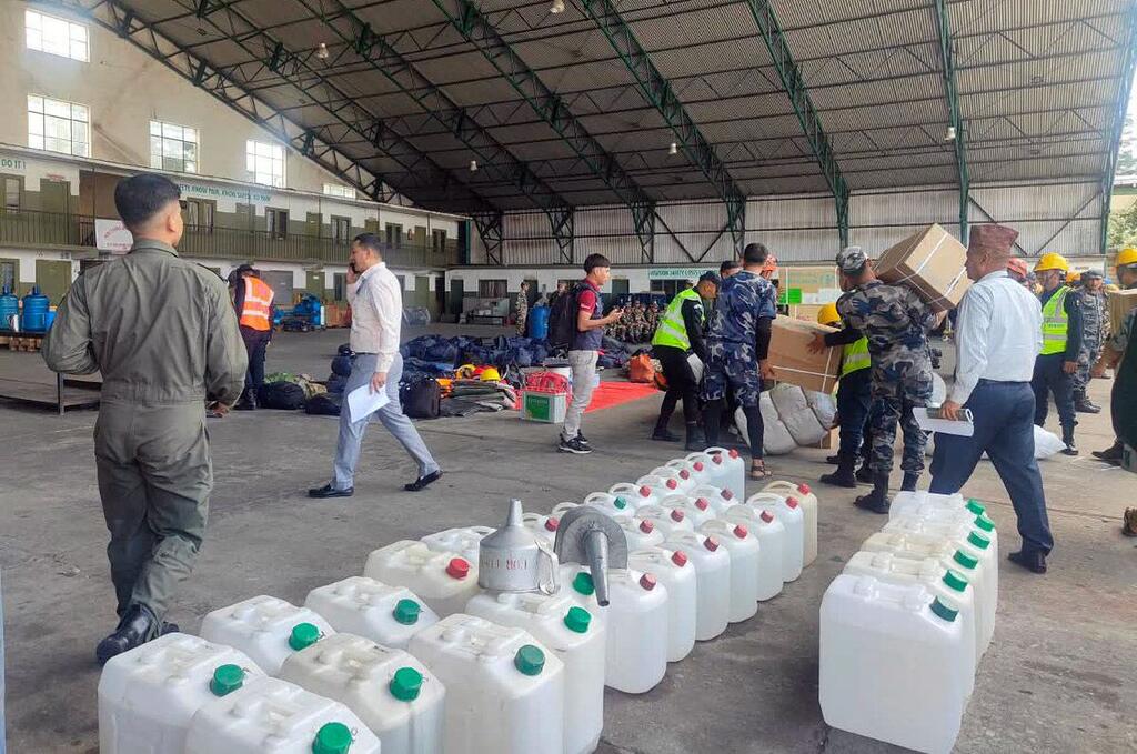 Dans un grand entrepôt de la zone de transit humanitaire de Katmandou, du personnel en uniforme et en civil manipule des jerricans en plastique blanc et des boîtes en carton lors du transport de fournitures d'abris d'urgence facilité par le PAM.