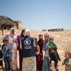Сотрудник WFP продовольственной программы в синем жилете с логотипом Всемирной продовольственной программы обращается к группе палестинских женщин и детей в Сада-эль-Таале, зоне C Западного берега, рядом с временными убежищами.