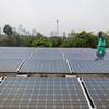 Un trabajador con uniforme y gorra verdes camina entre filas de paneles solares en la azotea de la mezquita Istiqlal, en el centro de Yakarta, con el brumoso horizonte de Yakarta y el Monumento Nacional visibles al fondo.