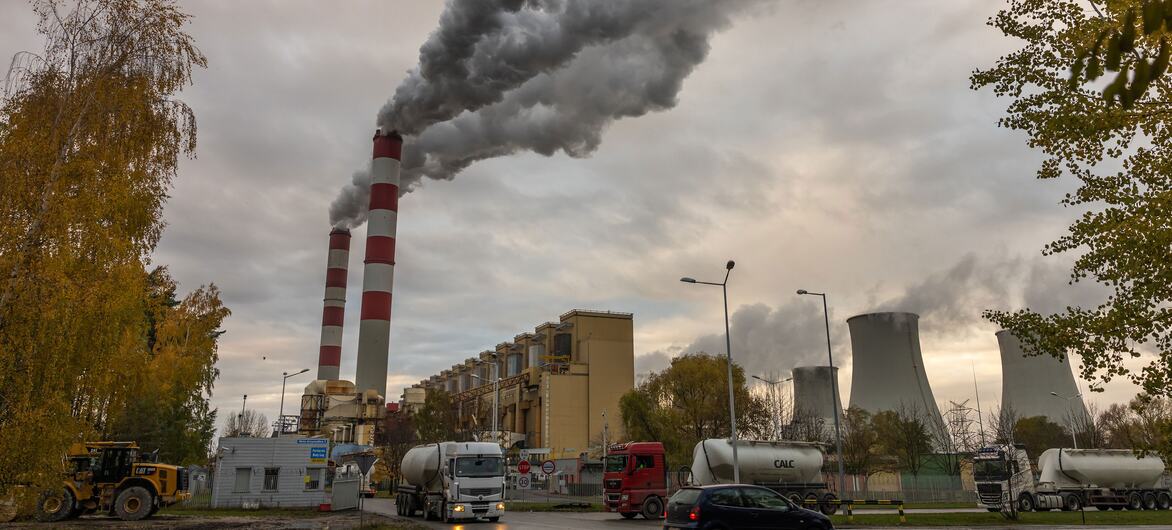 La central eléctrica de carbón de Belchatow en Rogowiec, Polonia, con chimeneas de rayas rojas y blancas que expulsan un humo oscuro y denso hacia un cielo nublado y torres de refrigeración de hormigón al fondo.
