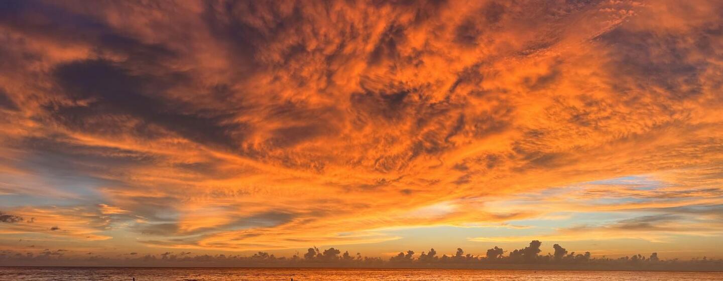 Vaste étendue océanique au coucher du soleil, avec des nuages ​​rouge orangé et orange flamboyant se reflétant à la surface de l'eau, illustrant des températures marines record dans le Pacifique tropical.