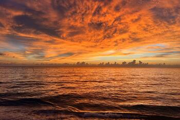 Vaste étendue océanique au coucher du soleil, avec des nuages ​​rouge orangé et orange flamboyant se reflétant à la surface de l'eau, illustrant des températures marines record dans le Pacifique tropical.
