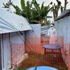 Un agent de santé en tenue de protection complète se tient derrière une barrière de sécurité orange sur un site d'extension d'un centre de traitement Ebola soutenu par l'OMS à Lita, avec des tentes portant les marques UNICEF et ALIMA visibles.