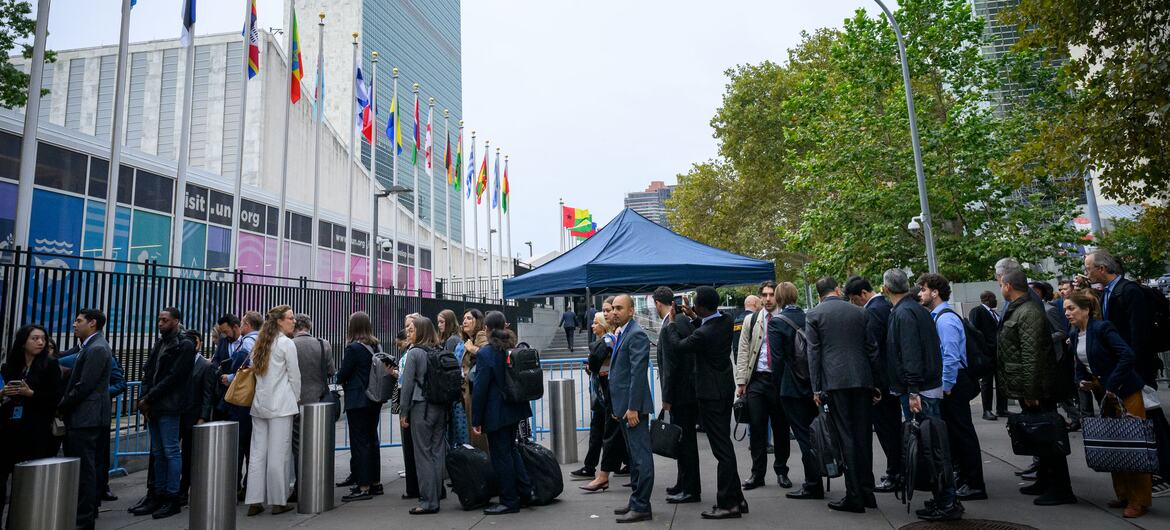 Des hommes et des femmes en tenue de ville arrivent au siège de ONU à New York, près des drapeaux nationaux et d'une tente bleue, le premier jour du débat de la 81e Assemblée générale.