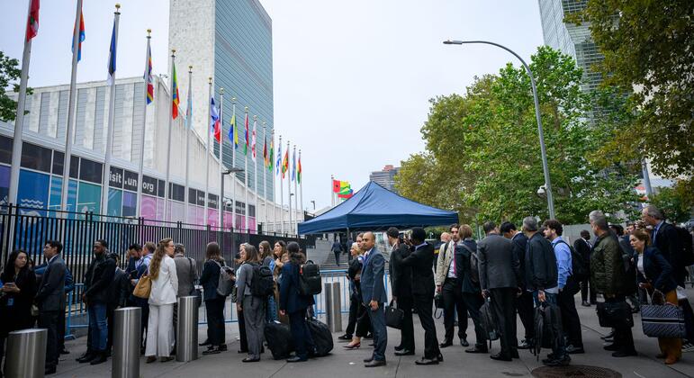 Men and women in business attire arrive at UN Headquarters in New York near national flags and a blue tent on the first day of the 81st General Assembly Debate.