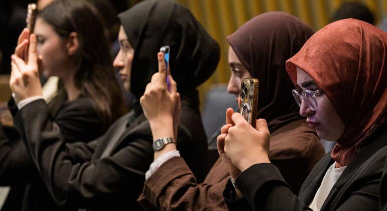 Young women, several wearing headscarves, hold smartphones to photograph a United Nations side event on protecting children in the digital world.