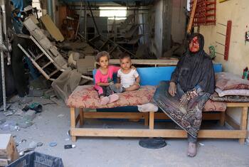 À Burij, dans la bande de Gaza, une femme blessée, coiffée d'un foulard noir, est assise pieds nus sur un matelas avec deux jeunes enfants à ses côtés, dans une pièce endommagée remplie de gravats et de débris.
