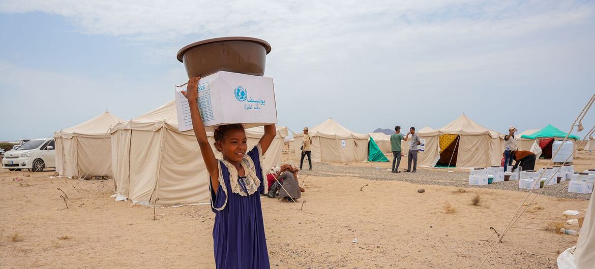Salimah Ahmed, a ten-year-old from Mocha, carries a box and basin overhead at Al-Firdoss IDP Center in Aden, Yemen, where UNICEF distributes emergency RRM kits to newly arrived families.
