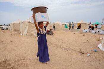 Salimah Ahmed, a ten-year-old from Mocha, carries a box and basin overhead at Al-Firdoss IDP Center in Aden, Yemen, where UNICEF distributes emergency RRM kits to newly arrived families.