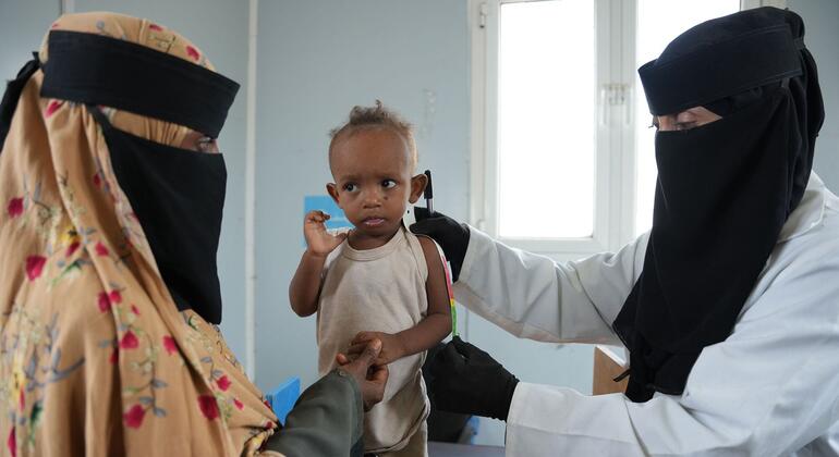 À Aden, dans une clinique, une agente de santé voilée en blouse blanche mesure le bras d'un petit garçon yéménite maigre à l'aide d'un ruban métrique, tandis que sa mère, également voilée, le tient dans ses bras.
