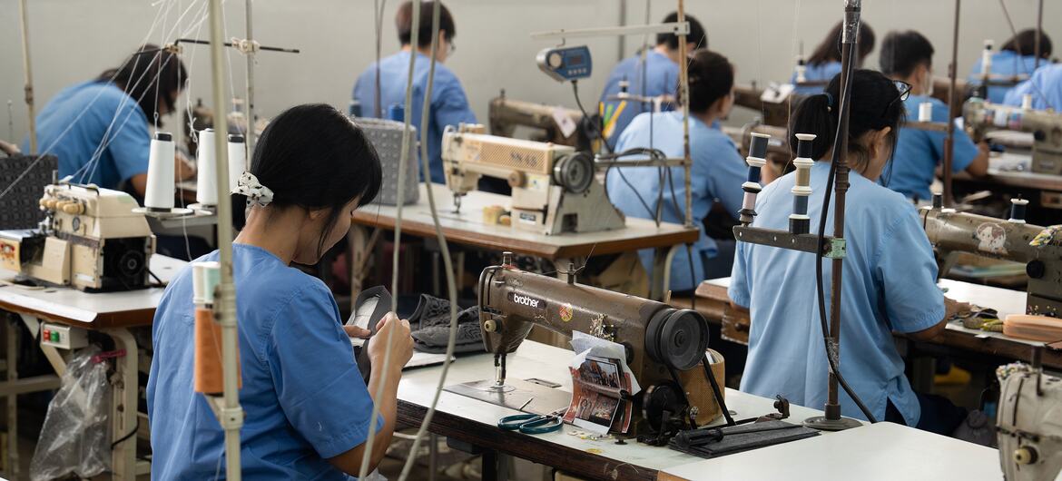 Thai female inmates in blue uniforms work at industrial sewing machines in a vocational training workshop inside a correctional facility in Thailand.