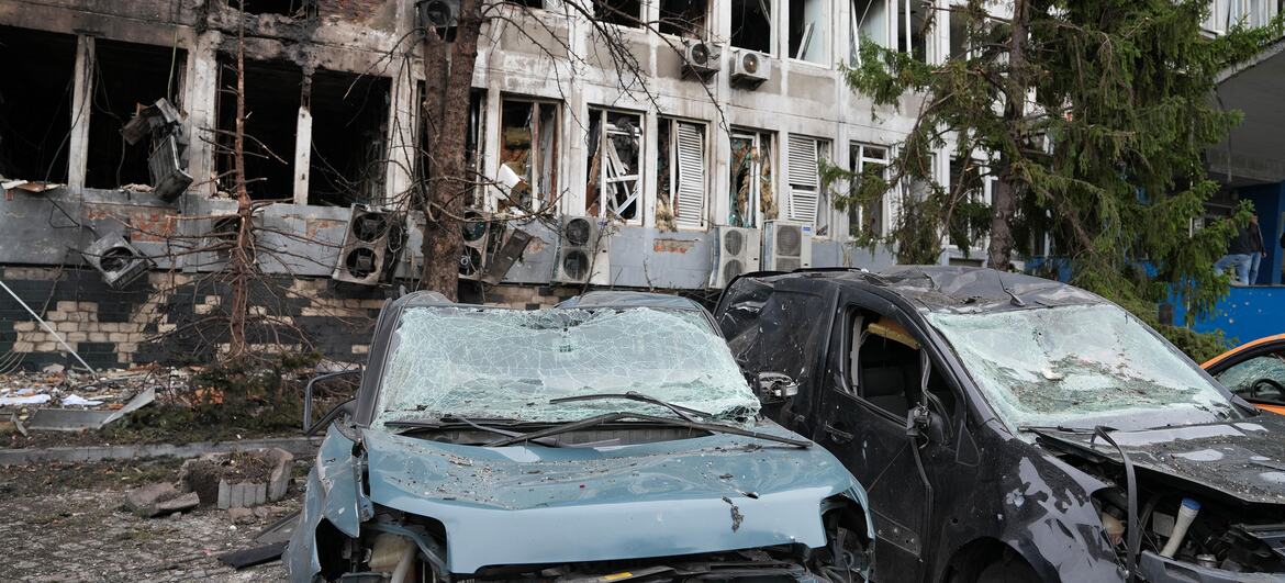 À Kyiv, en Ukraine, deux voitures accidentées gisent devant un immeuble de bureaux à plusieurs étages, aux fenêtres brisées et aux murs noircis par la suie.