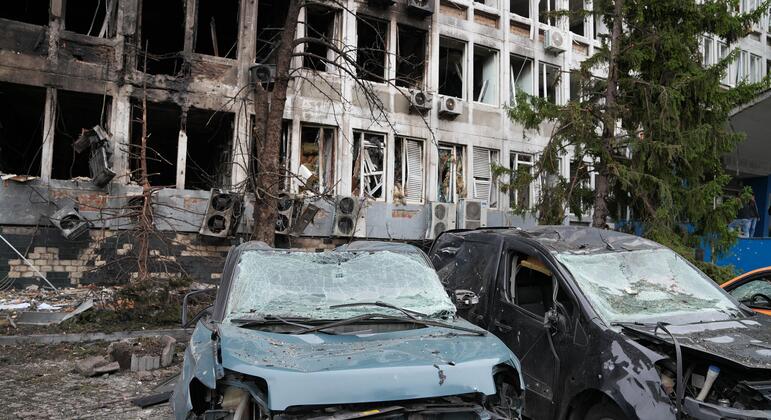À Kyiv, en Ukraine, deux voitures accidentées gisent devant un immeuble de bureaux à plusieurs étages, aux fenêtres brisées et aux murs noircis par la suie.