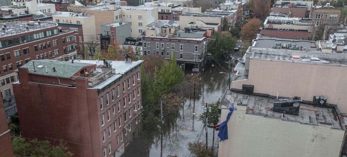 Vista aérea de uma rua residencial alagada na cidade de Nova York, com água submergindo carros estacionados entre prédios de apartamentos de tijolos após a Supertempestade Sandy.