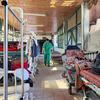 Un miembro del personal médico, vestido con uniforme quirúrgico verde, camina por un pasillo de un hospital abarrotado en Gaza, rodeado de camas y equipos médicos.