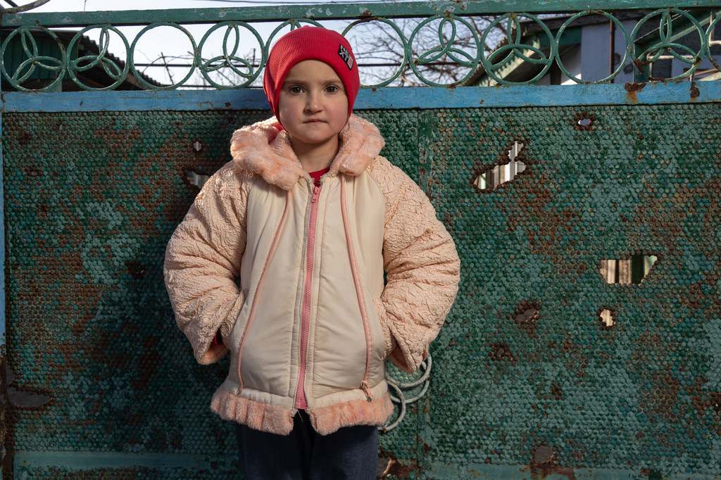 Alina, 12, stands next to her damaged home in Kobzartsi, Mykolaiv region.