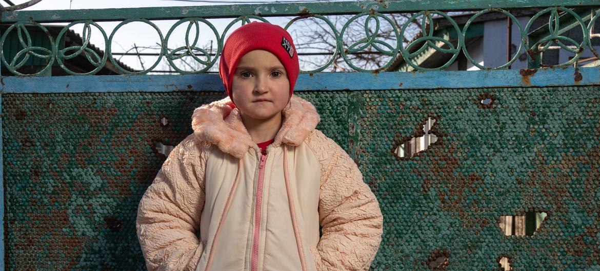 Alina, 12, stands next to her damaged home in Kobzartsi, Mykolaiv region.